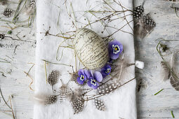 Easter egg with lettering, horned violets and feathers on linen cloth, 