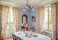 Oval table with vintage porcelain and floral curtains in the dining room