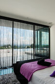 Schlafzimmer im Bungalow mit schwarzen Faden-Vorhängen und Blick auf die Terrasse