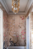 Gilded chandelier above hand-painted chinoiserie wallpaper mural with floral pattern