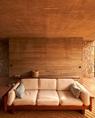 Wooden sofa with light-colored cushions in a rustic room made of natural stone and wood