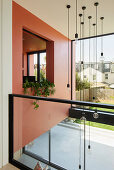 Modernes Haus mit korallenroter Wand, Glasgeländer und Pendelleuchte