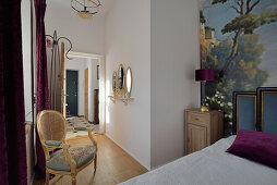 Schlafzimmer mit Wandgemälde und barockem Rattanstuhl