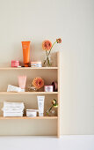 Shelf with cosmetic products and dahlias in glass vases