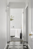 Hallway with chequered tiles and view of bright bathroom with free-standing bathtub