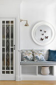 Bench with patterned cushions and round wall mirror with butterfly decoration