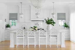 Elegant, white kitchen with island, striped curtains and plant arrangements