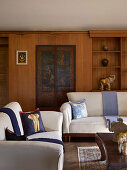 White sofa with elephant cushions in wood-panelled living room