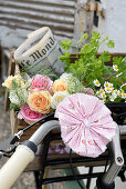 Homemade fabric rosette on bicycle handlebars and bouquet of roses, herbs and newspaper in the bicycle basket