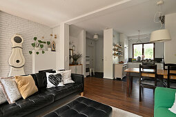 Open-plan living area with black leather sofa and white brick wall