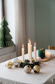 Adventskranz mit weißen Kerzen und goldenen Weihnachtskugeln auf Esstisch