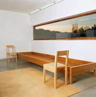 Zwei schlichte, moderne Holzstühle und ein langgestrecktes Holzgestell unter einem Fensterband