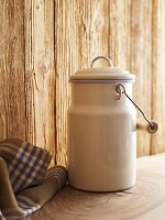 A milk churn in front of a wooden wall