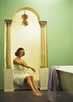 Eine Frau sitzt in der Nische eines orientalischen Badezimmers mit Säulen und Rundbogen