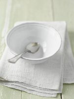 A white bowl with a spoon on a linen cloth