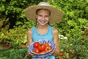 Mädchen hält Schüssel mit frischen Tomaten im Garten
