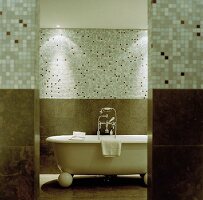 A free-standing, vintage-style bathtub with a mosaic-tiled wall