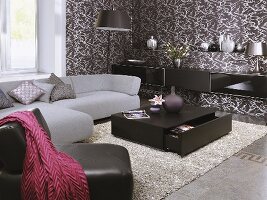 A grey sofa, a leather armchair and a black coffee table in a the corner of a living room with a brown and white papered wall