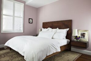 Schlafraum mit Doppelbett, hochgezogenem Kopfteil in Holzausführung & Nachtkonsole vor pastellrosa gefärbter Wand