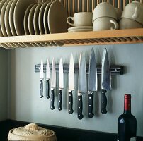 Cups and plates on a shelf above a magnet knife holder