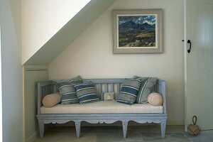 Wooden bench with blue striped cushions under sloping ceiling, painting on wall