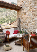 Terrace with wooden furniture and decorative cushions in front of a stone wall