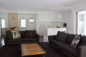 Modern living room with open-plan white kitchen and dark sofas