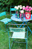 Retro garden table with roses in bottle vases and old metal chairs