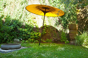 Yellow paper parasol, large stone basin and head of Buddha on lawn