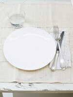 Place setting with white plate, cutlery and water glass