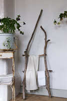 Towel holder made of branches next to weathered table with plant