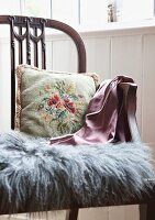 Floral embroidered cushion and grey fur mat on antique, English-style wooden chair