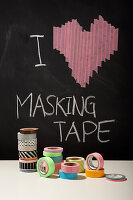 Colourful masking tape rolls in front of blackboard with heart motif and lettering