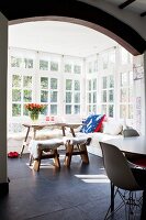 Gemütliche Eckbank mit Schaffellen, Holztisch und Hockern im Wintergarten mit Sprossenfenstern