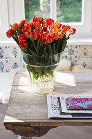 Glass vase of orange and red tulips on rustic wooden table