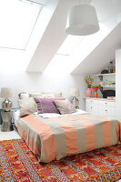 Double bed in white attic room with orange-colored accents
