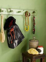 Grüne Badezimmerwand mit hölzerner Hakenleiste mit daran hängendem Schmuck und einem selbgenähten Stoffsack; darunter ein antiker Beistelltisch