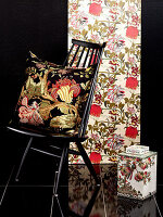 Cushion with floral cover on chair in front of black wall with strip of patterned wallpaper