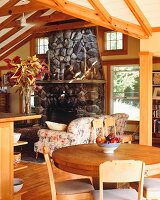 Esstisch mit Stühlen aus Holz und Loungebereich vor offenem Kamin in Natursteinwand eines Wohnzimmers im Landhausstil