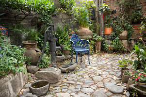 Rustikaler Garten mit Steinboden, Wasserpumpe und blauem Stuhl