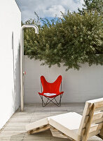 Roter Sessel und Liegestuhl auf Holzterrasse