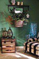 Striped armchair, fairy lights in glass vessels, demijohns on side table and basket of Christmas decorations on green wall