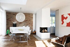 Open-plan interior with dining area, free-standing fireplace block and herringbone parquet floor; exposed brick wall behind dining area
