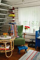 Rattan side table, green armchair and blue footstool in rustic interior of wooden house