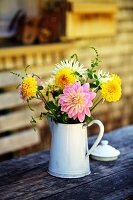 Dahlias in old, white enamel jug on outdoor table