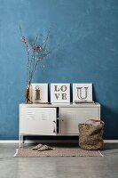 Vintage arrangement of white locker against blue-grey wall and three DIY string art pictures
