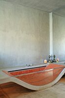 Bathtub made from curved concrete slab and glass side wall with red mosaic tiles inside in minimalist bathroom