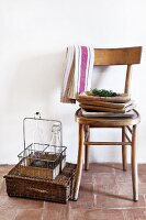 Wooden dishes stacked on wooden chair against white wall; bottle carrier standing on wicker case