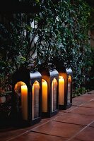 Close-up of candle lanterns in a row on tiled floor by plants