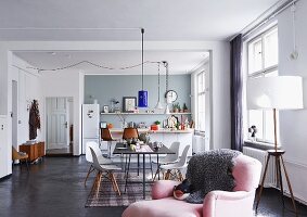 Open-plan interior with kitchen, dining area with classic chairs and pink armchair in foreground